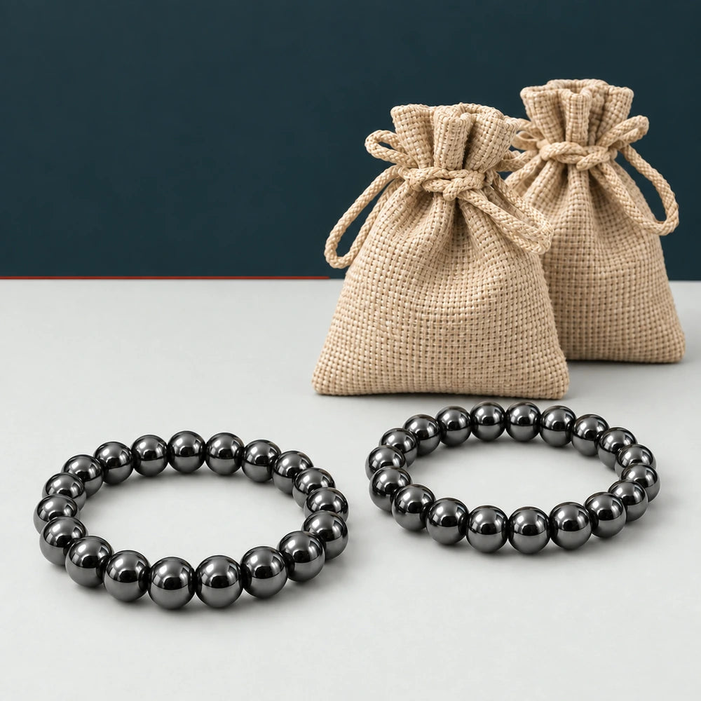 Dos pulseras de hematita natural con bolsas beige sobre fondo mineral grafito
