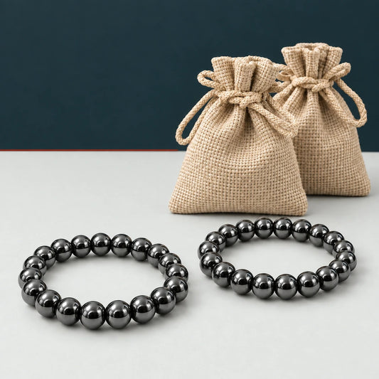 Dos pulseras de hematita natural con bolsas beige sobre fondo mineral grafito